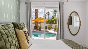 A bedroom with a bed, a large window, and a view of a pool and outdoor seating.