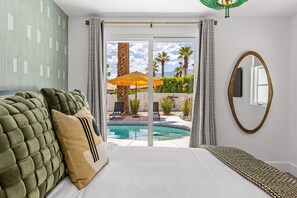 A bedroom with a bed, a large window, and a view of a pool and outdoor seating.