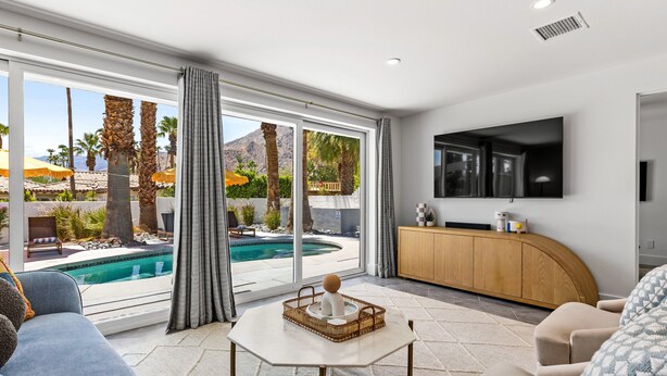 A modern living room with a pool view, a flat-screen TV, and a wooden cabinet.