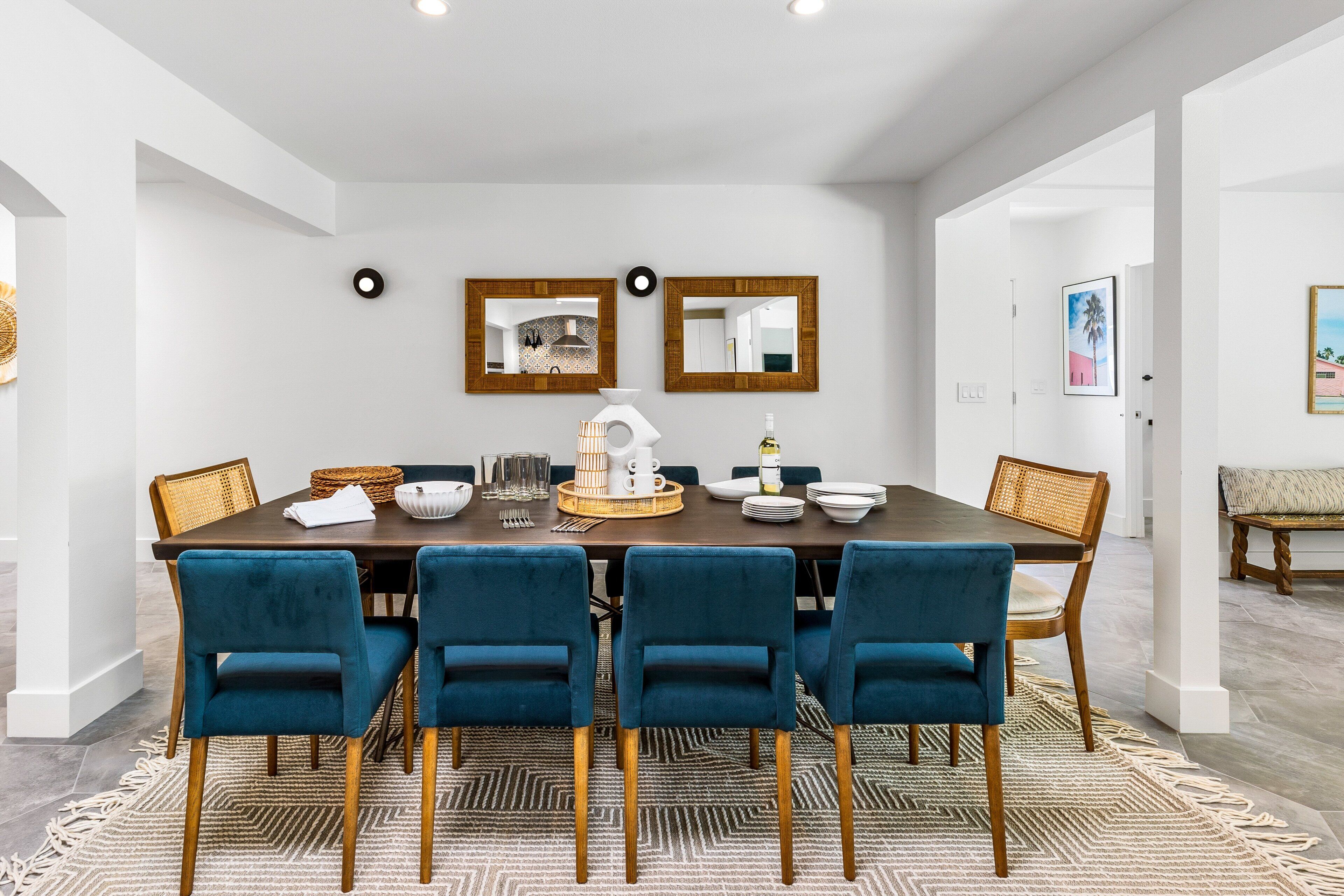Un coin repas avec une table en bois foncé, des chaises en velours bleu et un plateau décoratif en fibres tressées au centre.