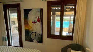 Una habitación con cama, una silla, un cuadro y una ventana con vista al mar.