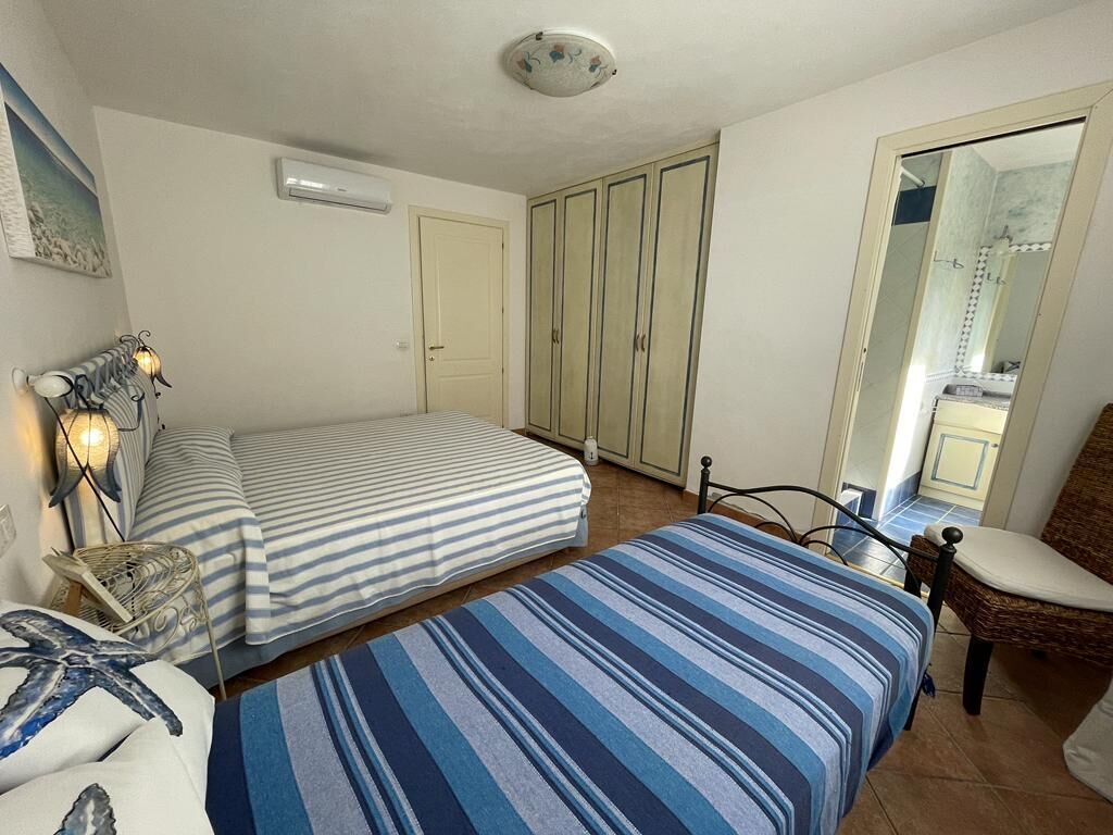 A bedroom with two beds, a chair, a radiator, a wardrobe, and a mirror.