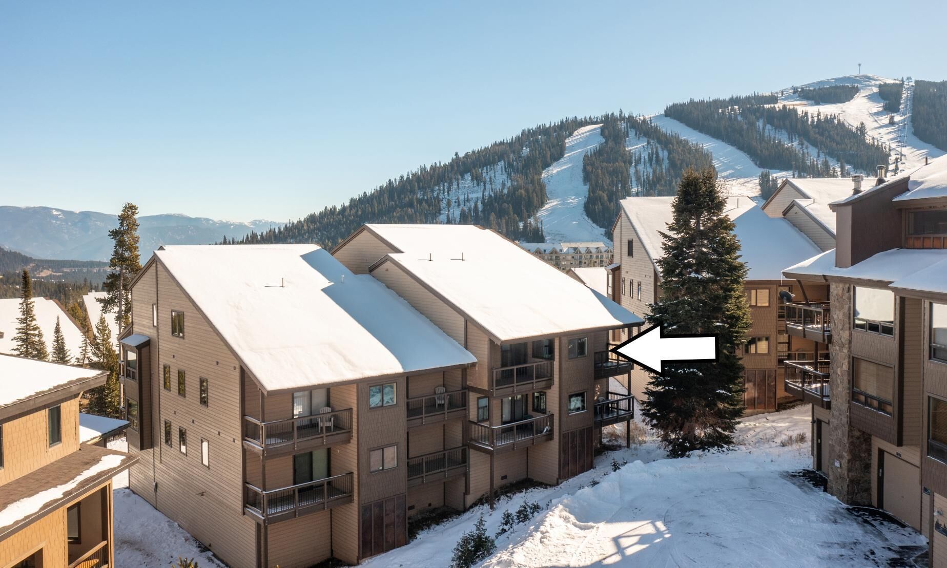 Un edificio moderno de varios pisos con balcones, rodeado de nieve y una pista de esquí al fondo.