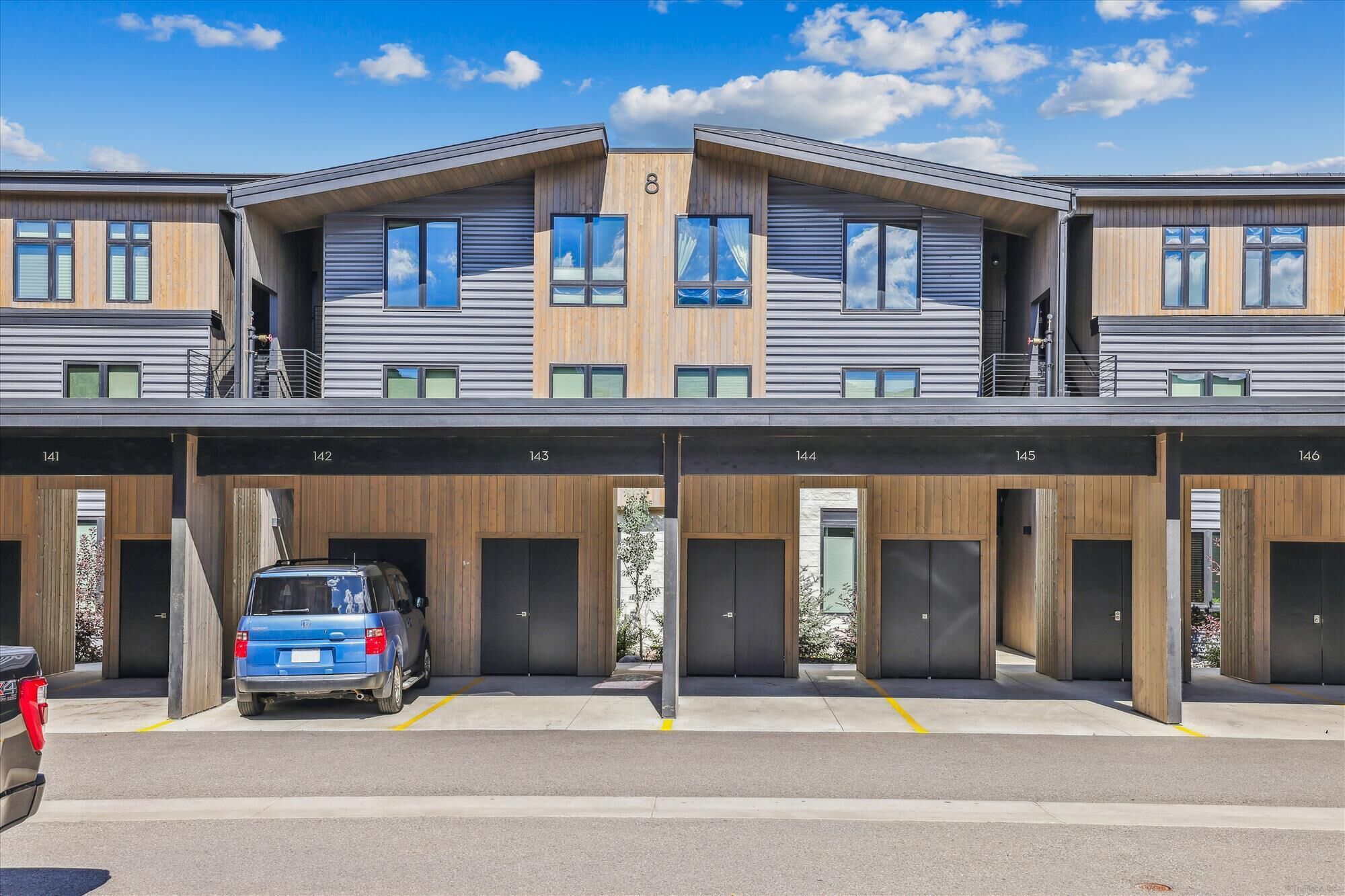 A modern building with multiple garage doors, numbered 141 to 146, and a blue car parked in front.