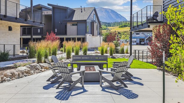 A modern outdoor seating area with Adirondack chairs and a fire pit, surrounded by landscaped gardens and a view of a mountain. - River West 814-Riverfront Silverthorne Condo, Fireplace, Hot Tub, Private Patio (Silverthorne)