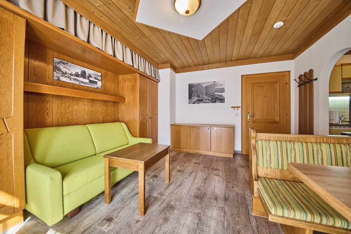 A cozy room with a wooden ceiling, a green sofa, a wooden bench, and a small table.