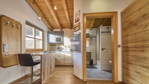 A modern kitchen with wooden beams, a bar area, and a view of the mountains. - Landhaus Eichenhof (Saalbach-Hinterglemm)