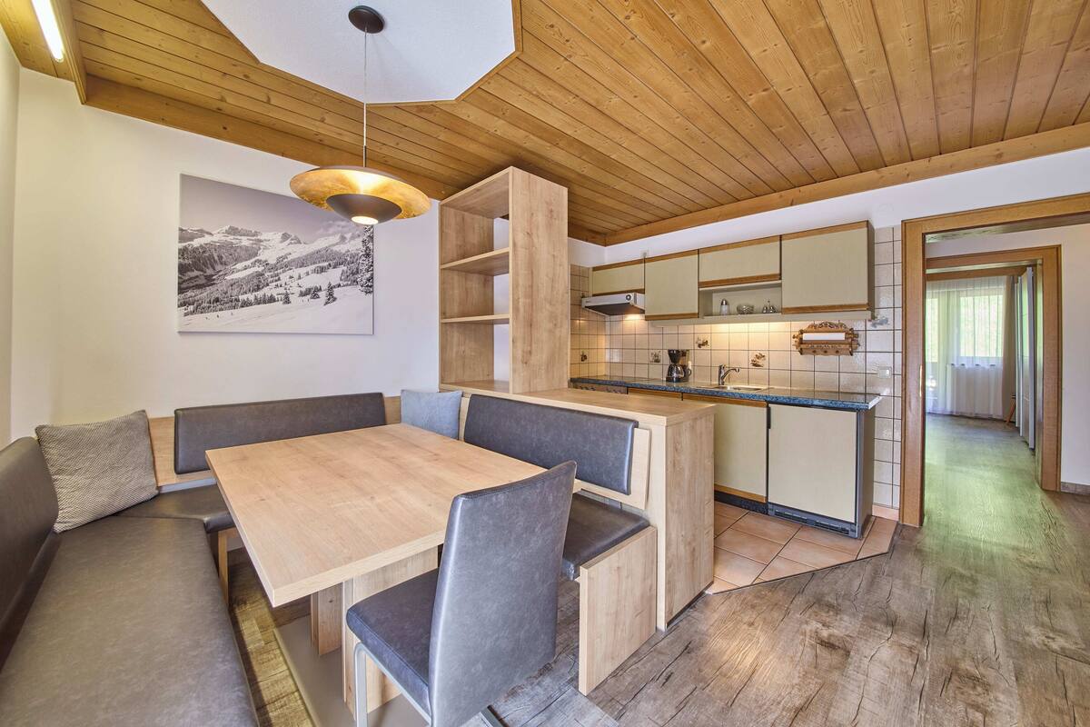 A modern kitchen with wooden cabinets, a built-in island, and a dining area with a wooden table and cushioned seating.