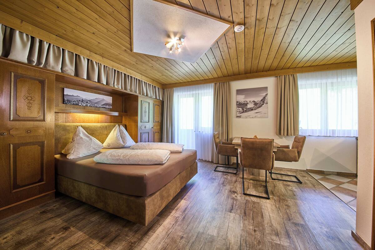 A hotel room with a wooden ceiling, a large bed, a desk, and a chair.