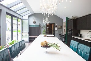 A modern kitchen with a central island, a chandelier, and a view through the glass doors.
