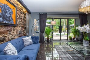 Una sala de estar moderna con un sofá azul, una pared de piedra, un ventanal grande y una mesa de centro de vidrio.