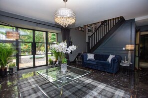 Un salon moderne avec une table basse en verre, un canapé bleu, un lustre et un escalier.