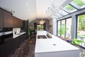 Une cuisine moderne dotée d’un îlot central, d’un sol en marbre foncé et d’une grande fenêtre donnant sur un jardin.