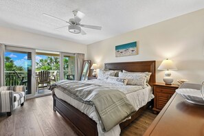 Un dormitorio con cama, dos lámparas de noche, ventilador de techo, mesita de noche, una silla y vistas al exterior.