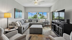 A modern living room with a sectional sofa, ottoman, TV, and ceiling fan. - Oceanfront Villa w/ Private 2nd Floor Balcony (Hilton Head Island)