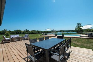 Relax by the pool with a view of the lake from this outdoor deck, featuring a table, chairs, umbrellas, and lounge chairs.