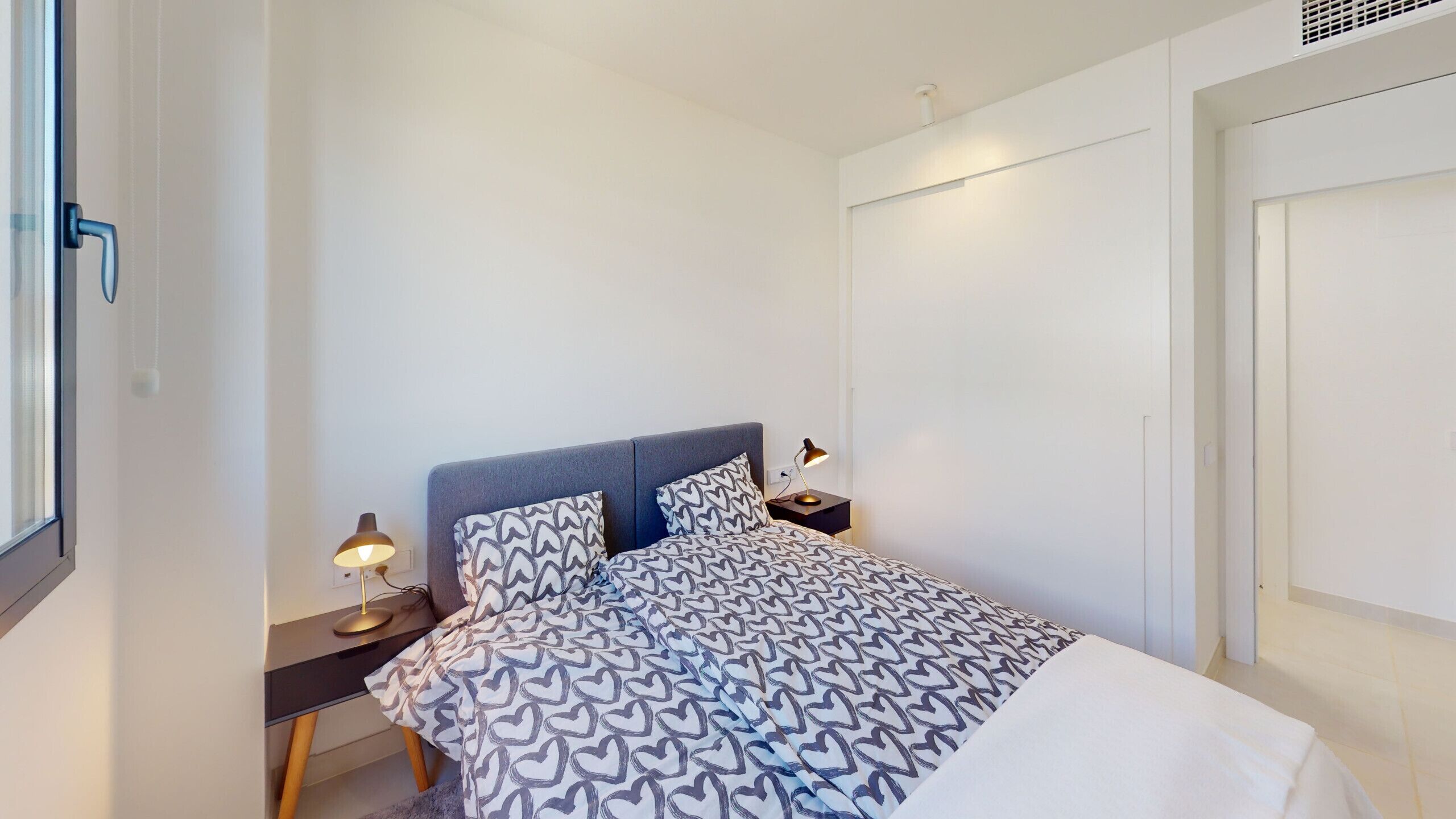 Een slaapkamer met een bed, bedlampen, een nachtkastje en een raam.