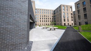 A modern building with a brick facade, a paved walkway, and outdoor seating areas. - University of Galway Rooms (Galway)
