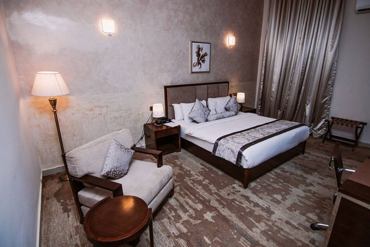 A hotel room with a large bed, a sofa, a small table, and a nightstand with lamps.