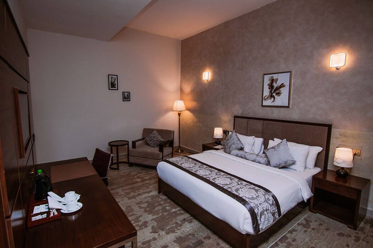 A hotel room with a large bed, bedside tables, a desk, a chair, and a lamp.
