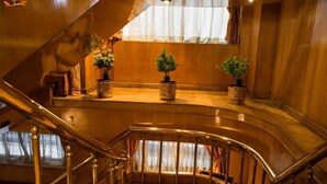 A wooden staircase with a curved design, leading to a landing area with three potted plants. - GTS Nile Cruise  (Aswan)