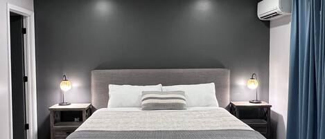 A modern bedroom with a large bed, two bedside tables with lamps, a ceiling fan, and an air conditioning unit.