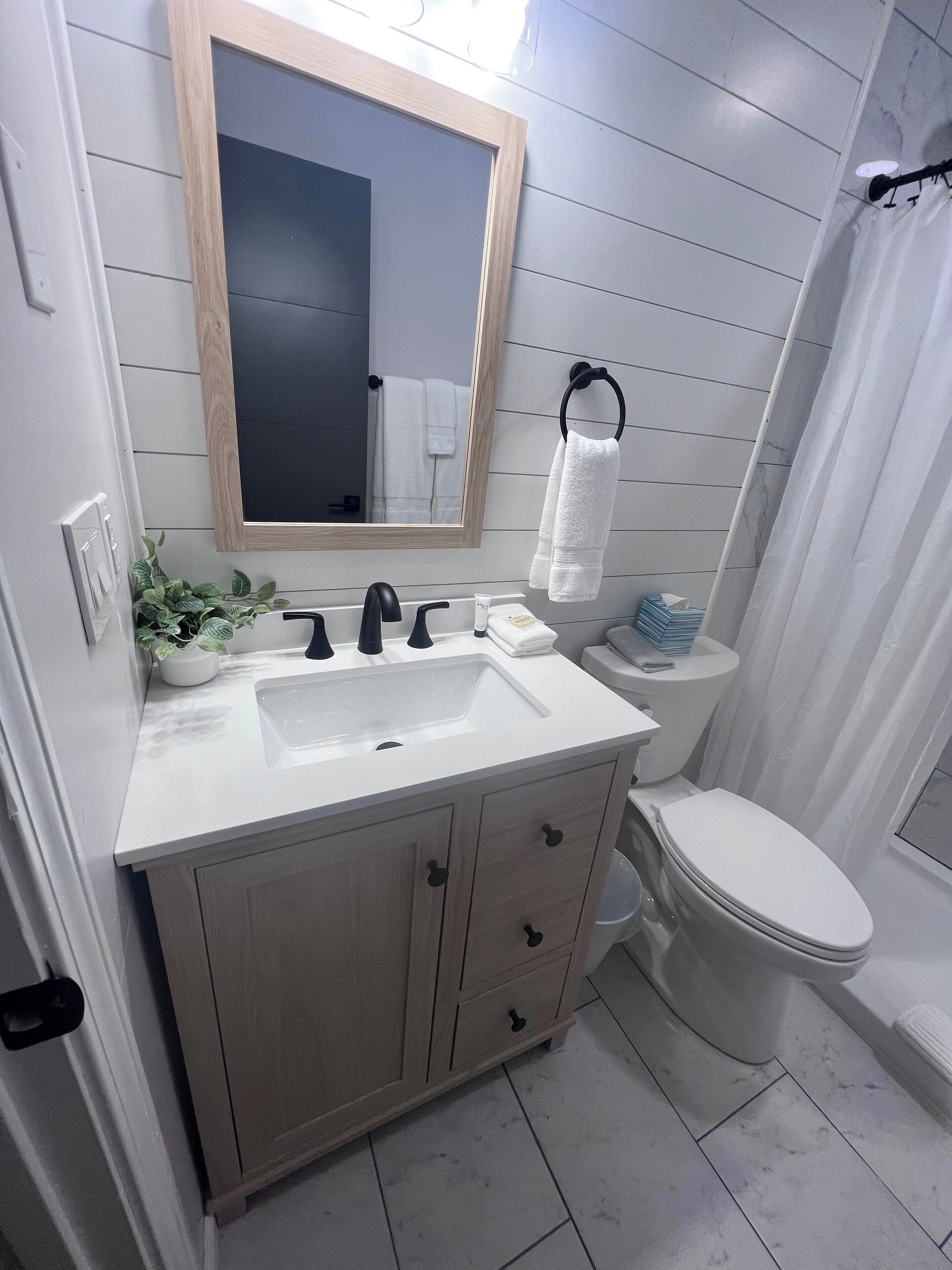 A bathroom with a white sink, mirror, and toilet. There is a plant on the sink counter and a towel hanging on the wall.