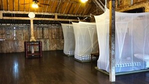 A rustic room with wooden floors, a wooden ceiling, and four beds with mosquito nets. - Seabreeze Hostel Bali (Canggu)