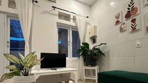 A modern living room with a flat-screen TV, a wooden coffee table, a green sofa, and a potted plant. - Seabreeze Hostel Bali (Canggu)