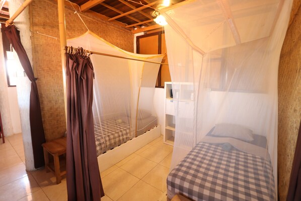A room with two beds, one with a canopy and one without, a small wooden stool, and a brick wall.