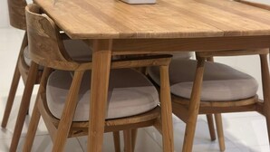 A wooden dining table with cushioned chairs, surrounded by potted plants. - Seabreeze Hostel Bali (Canggu)