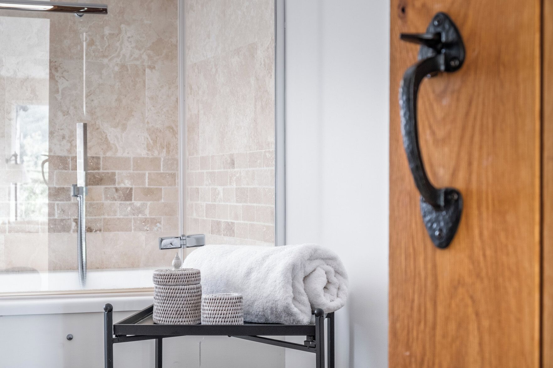 Un baño con cabina de ducha de vidrio, una puerta de madera con pomo negro y una toalla en un perchero.