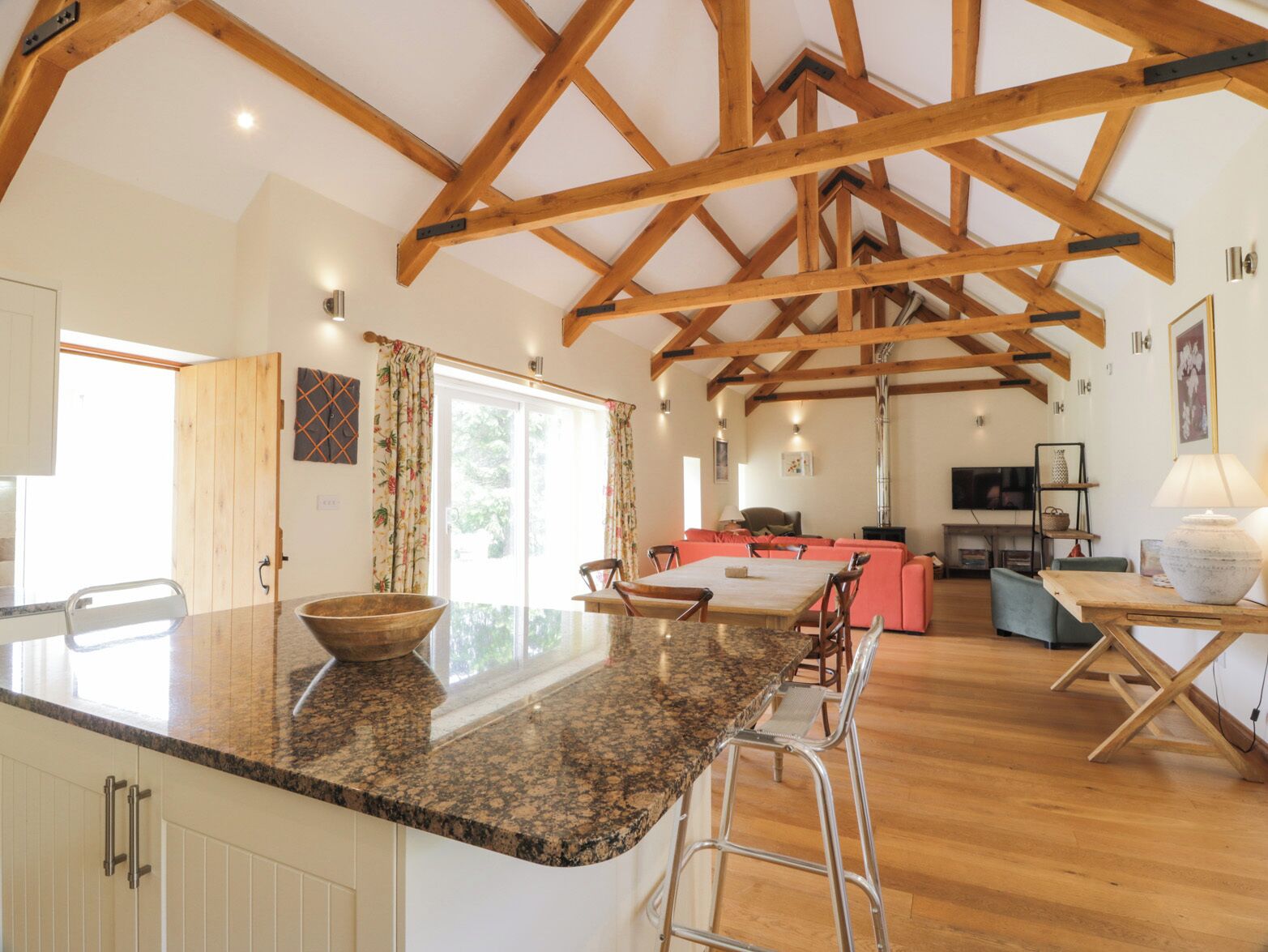 A spacious kitchen with a granite countertop, wooden beams, and a large window.