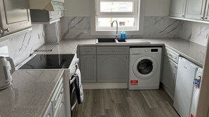 A compact kitchen with a built-in washer and dryer, a sink, and a window providing natural light. - Cosy Cottage Apartment (Argyll and Bute Council)
