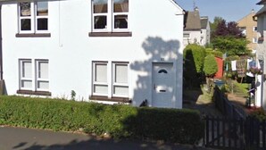 A two-story white house with a red roof, multiple windows, and a visible chimney. - Cosy Cottage Apartment (Argyll and Bute Council)