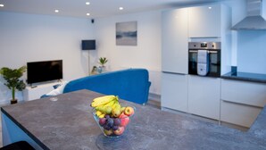 A modern kitchen with a built-in oven and a dining area with a fruit bowl on the counter. - Spacious & Modern 2-Bedroom House (Worksop)