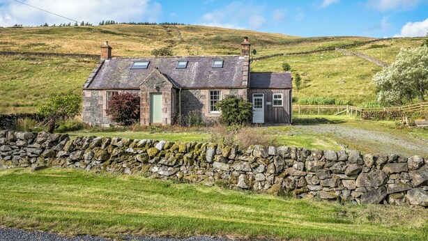 A stone house with a sloped roof, a small attached shed, and a stone wall in front. - Prince's Cottage (Thornhill)