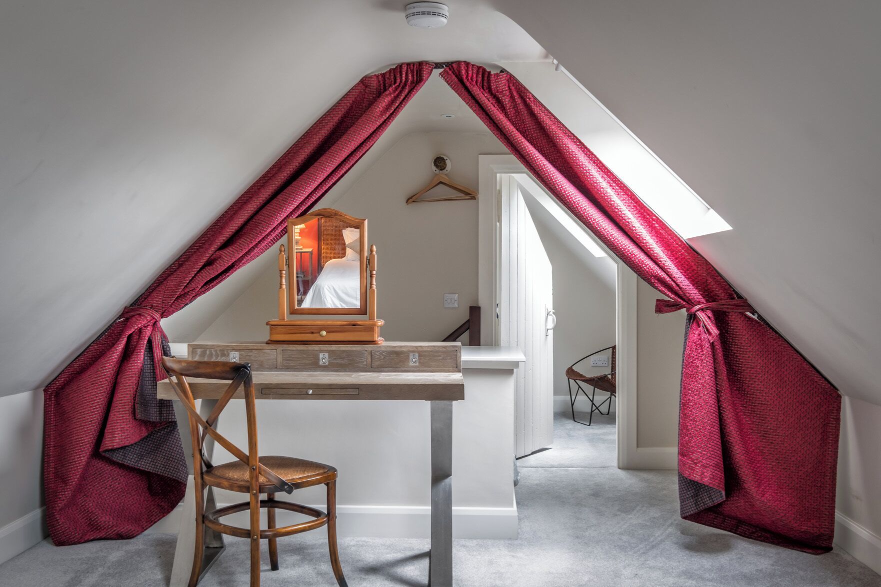 Une petite chambre mansardée avec une commode en bois, une chaise et un miroir.