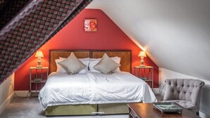 A bedroom with a sloped ceiling, a bed with white linens, two bedside tables with lamps, a chair, and a small table with a tray. - Prince's Cottage (Thornhill)