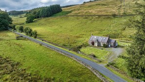 A rural landscape with a stone house on a hill, surrounded by fields and a winding road. - Prince's Cottage (Thornhill)