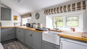 A modern kitchen with grey cabinets, a wooden countertop, a built-in dishwasher, and a window with a view of the garden. - Prince's Cottage (Thornhill)
