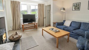 A cozy living room with a fireplace, a television on a wooden stand, a blue sofa, and a wooden coffee table. - High Auchenbrack (Thornhill)