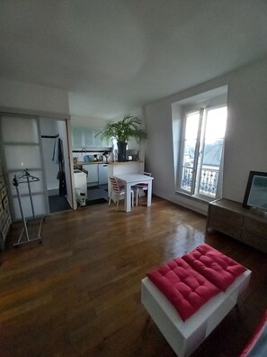 An open-plan living space with a dining area, a red cushioned bench, and a large window with a view. - Appartemement aux Batignolles (Paris)