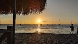 Une plage au coucher du soleil, avec des bateaux et des gens qui se promènent.