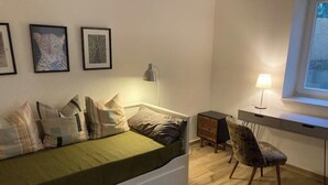 A bedroom with a bed, a desk, a chair, and a window.