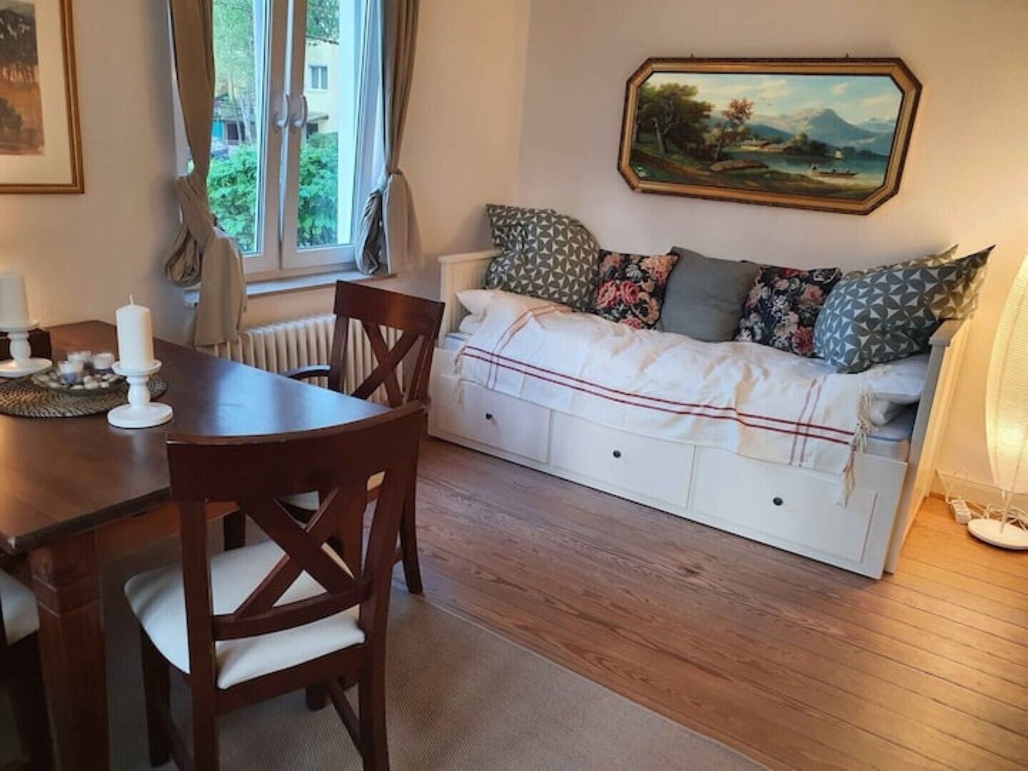 A cozy room with a wooden dining table, chairs, a white sofa with patterned cushions, and a painting on the wall.