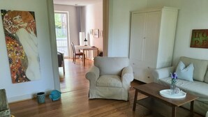 A living room with a sofa, armchair, and a coffee table. There is a painting on the wall and a door in the background. - Living in the Mayor‘s Mansion (Hamburg)