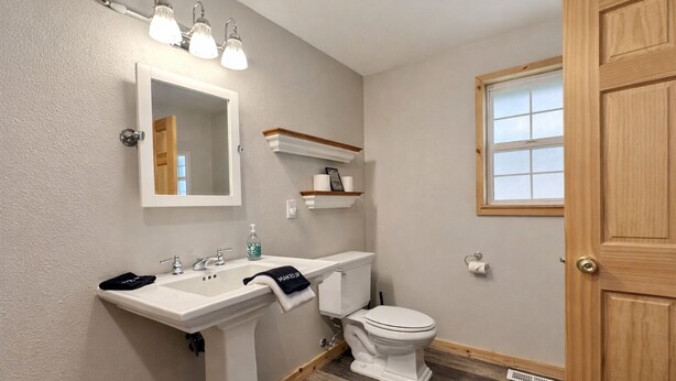 A bathroom with a white sink, a toilet, and a mirror. There are three light fixtures above the mirror. - River Road Lodge 7 Bedroom Lodge by NW Comfy Cabins by RedAwning (Leavenworth)