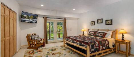 A bedroom with a bed, a wooden chair, a TV, and a door leading to a balcony.