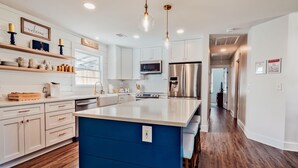 A modern kitchen with white cabinetry, a blue island, stainless steel appliances, and pendant lighting.